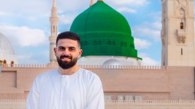 man in white long sleeve shirt standing near a mosque